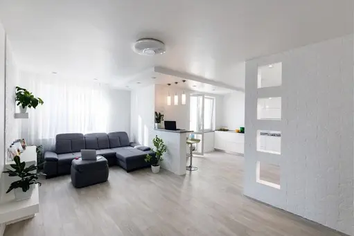 Salón reformado con sofá gris, cocina abierta y luz natural